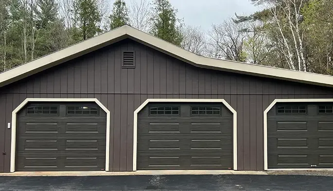 A brown garage with three dark garage doors framed in beige.